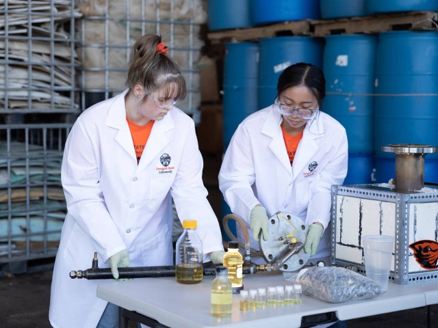 two researchers in a lab coats load plastic into kiln reactor